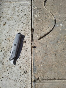 Removing old, cracked pool mastic from a concrete expansion joint using a utility knife to prepare for repair.